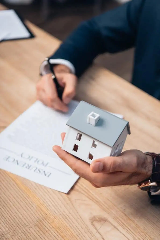 cropped view of lawyer holding house model near documents with insurance policy lettering on table